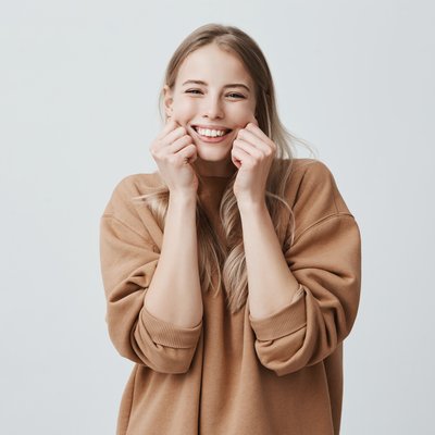 charming-beautiful-female-model-smiling-broadly-wearing-brown-sweater-pinching-her-cheeks-mocking-having-good-mood-fun-positive-emotions-feelings