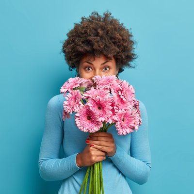 good-looking-delicate-african-american-woman-smells-rosy-gerbera-flowers-enjoys-pleasant-odour-holds-bouquet-hands